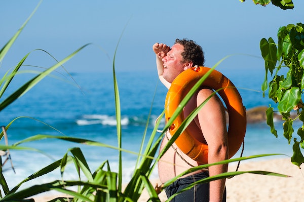 A man on a beach,
    with a life-preserver over his shoulder. He appears to be looking for
    something.