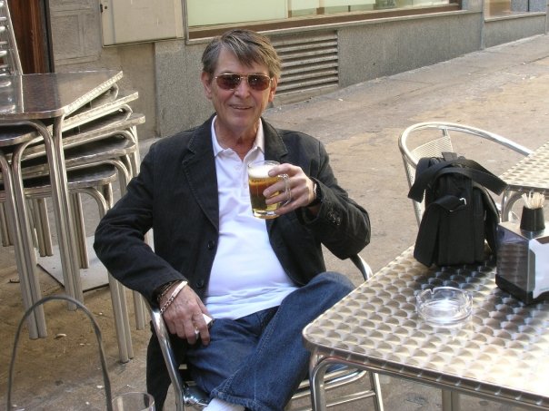 A middle-aged
    man, smiling and sitting at an outdoor café in Toledo, Spain. He’s
    enjoying a beer.